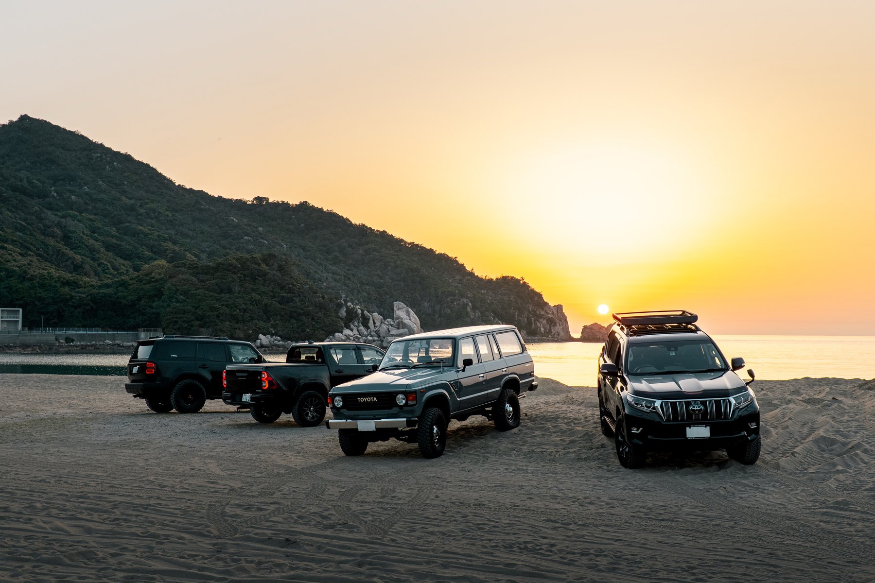夕暮れの海辺に集まったハイラックスなど四台の車
