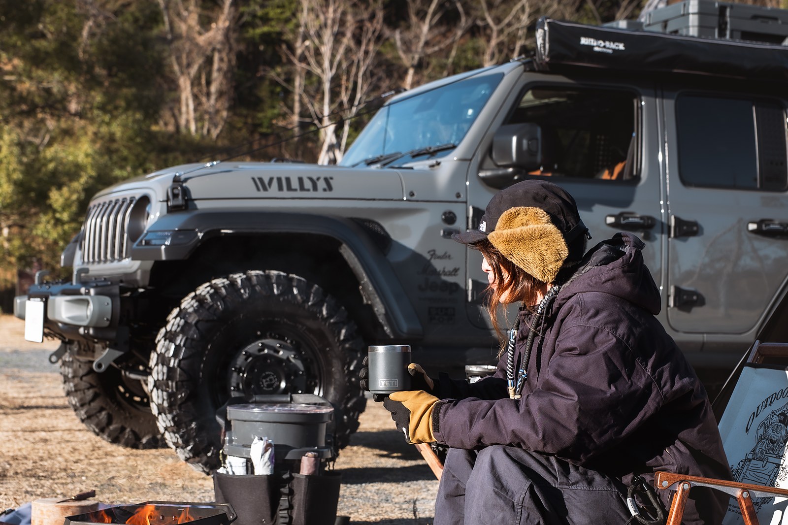 Willys Jeepの横で焚き火を囲む冬キャンプ、Yetiマグで温まる村谷さん