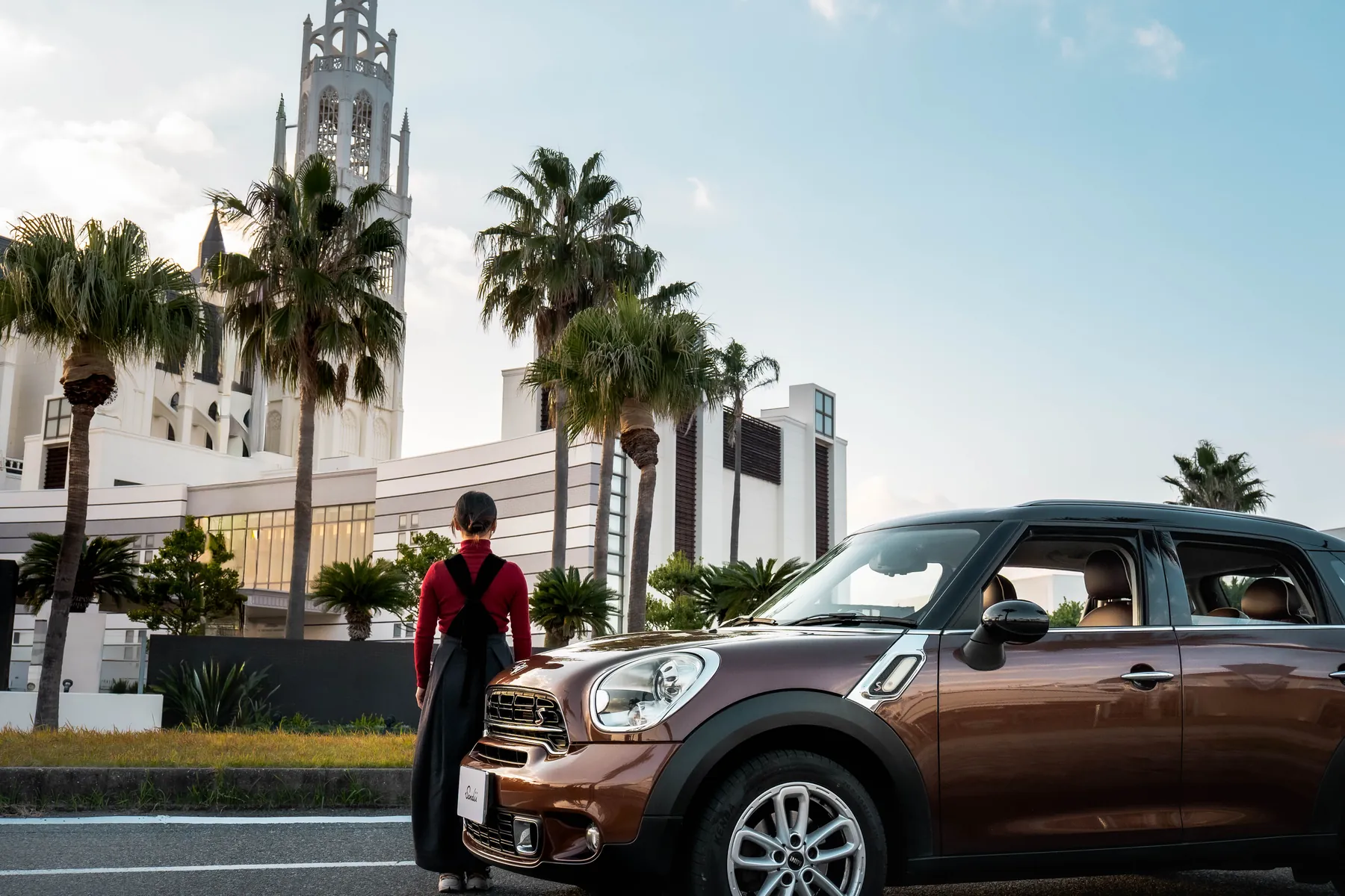 夕暮れの街に停車したブラウンのMINI 5ドアと人物